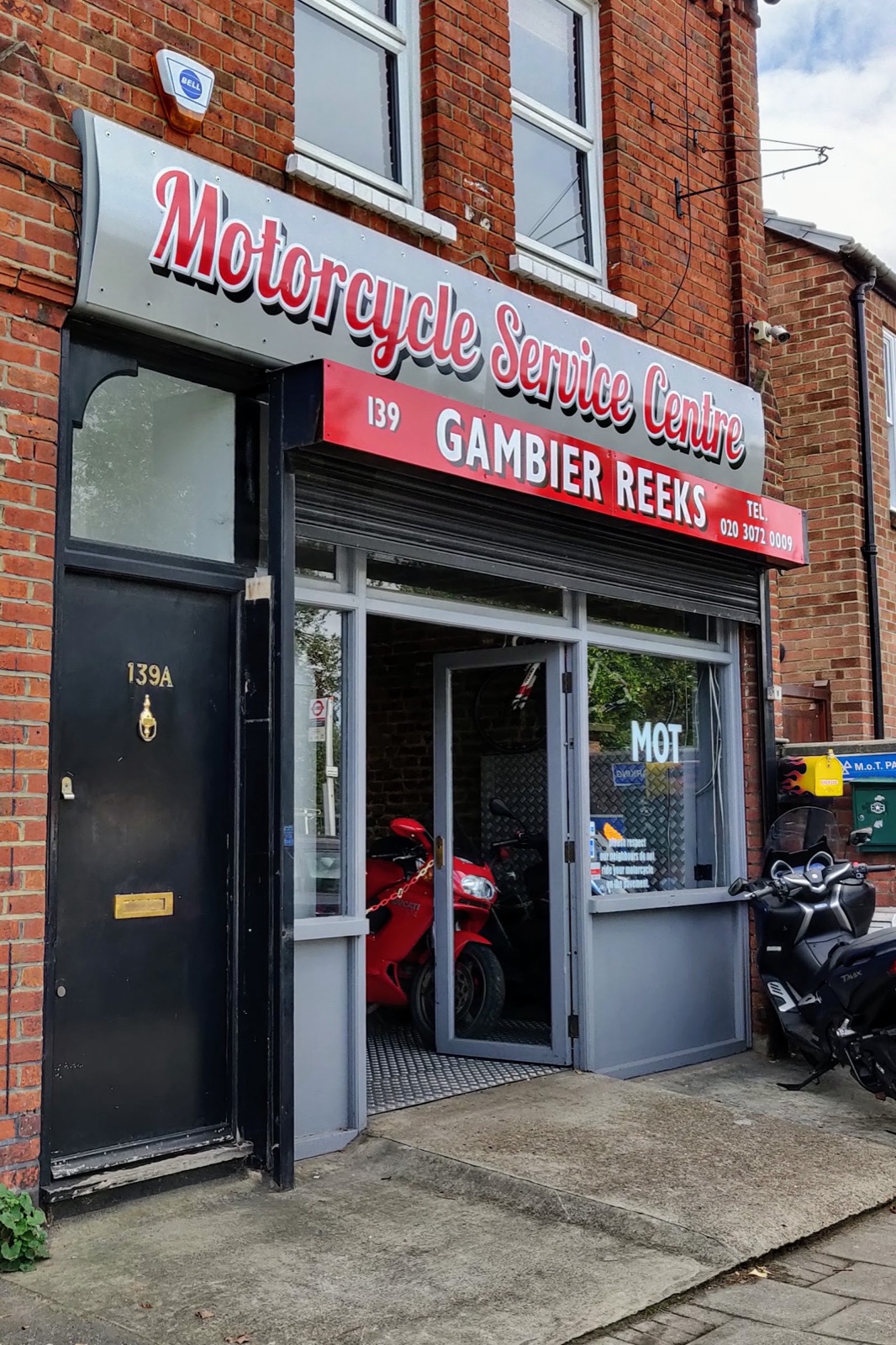 A white Rolls-Royce raised on the ramp inside Gambier Reeks on Putney Bridge Rd, under the workshop sign